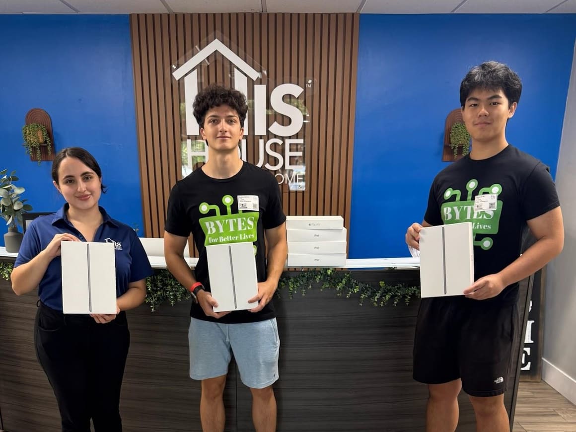 Three volunteers holding donated iPads at the front desk of His House Children’s Home
