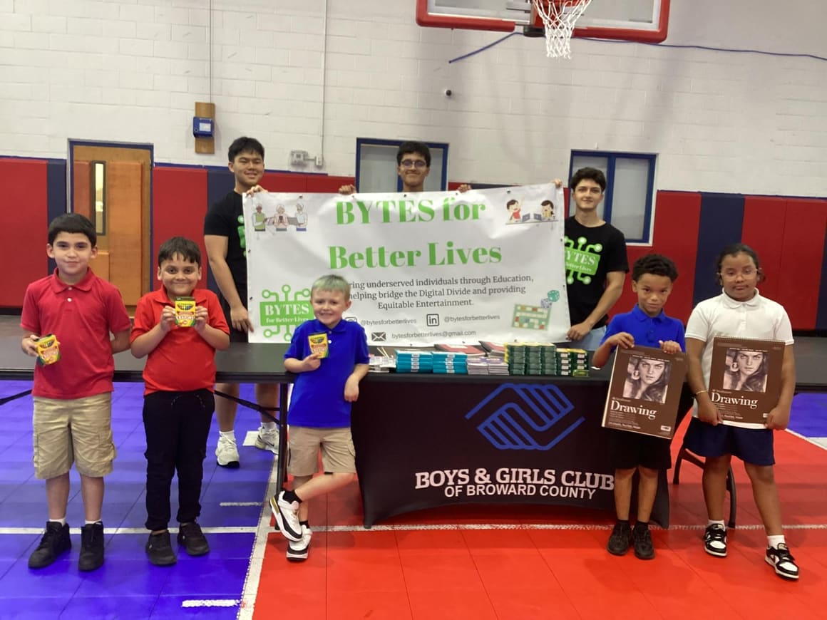 Volunteers and children holding donated drawing books and games in a Boys & Girls Club gym